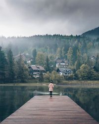 Rear view of man standing on pier over lake against sky