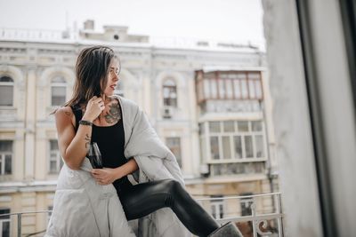 Woman with wineglass wearing blanket while standing at balcony during winter