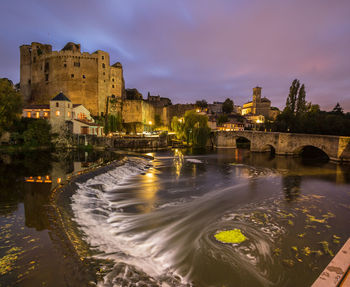 Illuminated buildings by river against sky at dusk