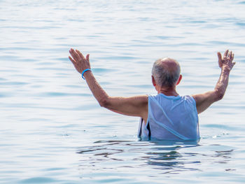 Rear view of senior man with arms outstretched standing in sea