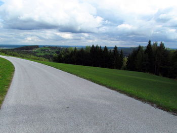 Road passing through field against cloudy sky