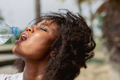 African woman hydrating and drinking water from a bottle on a hot day outdoors.