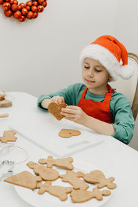 A cute boy in a santa hat stretches a rope into the hole of a ginger cookie in the shape of a heart