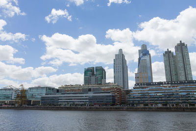 Modern buildings by river against sky in city