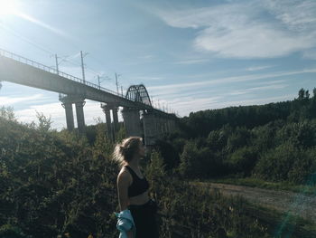 Side view of woman standing on bridge against sky