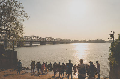 People on bridge over river against clear sky