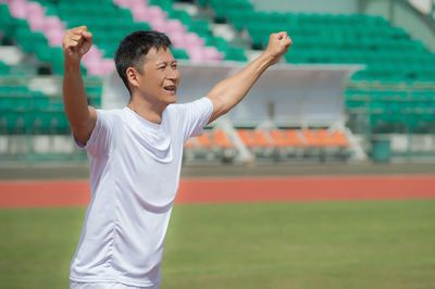 Happy sportsman with arms raised walking on field