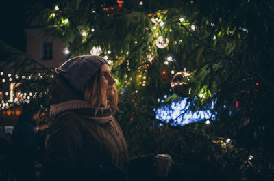 Woman on illuminated christmas tree at night
