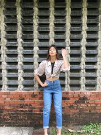 Portrait of young woman standing against brick wall