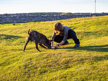 Full length of mature woman playing with dog on grass