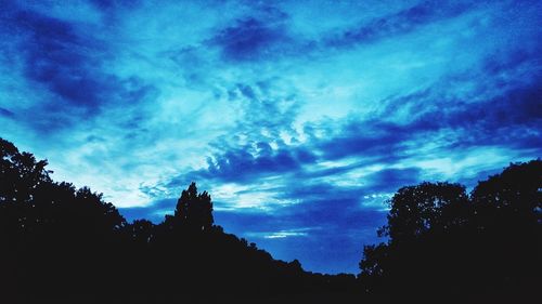 Low angle view of silhouette trees against dramatic sky