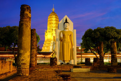 Statue amidst illuminated buildings against sky