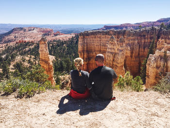 Rear view of couple  sitting on rock against mountains