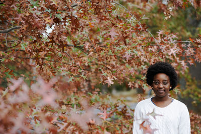 Portrait of smiling young woman standing by trees during autumn