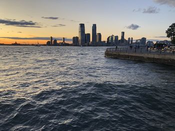 Sea by buildings against sky during sunset