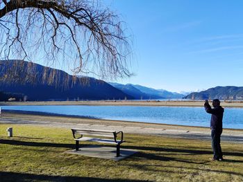 Side view of man standing on land by lake against sky