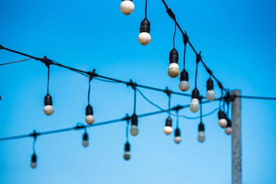 Low angle view of light bulbs hanging against blue sky