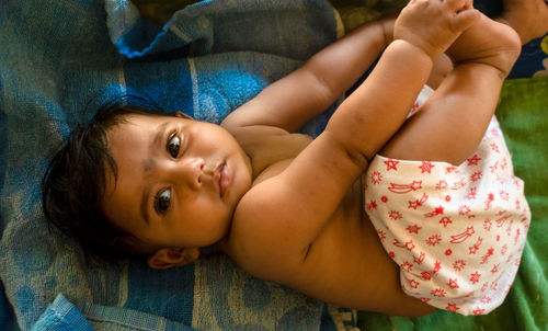 Cute indian baby lying on a blue towel holding her feet looking away from camera. selective focus 