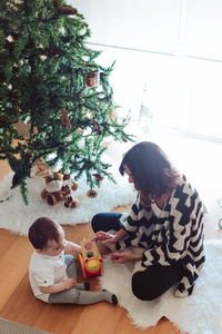 Rear view of girl sitting by christmas tree on floor