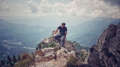 Full length of man sitting on cliff against sky