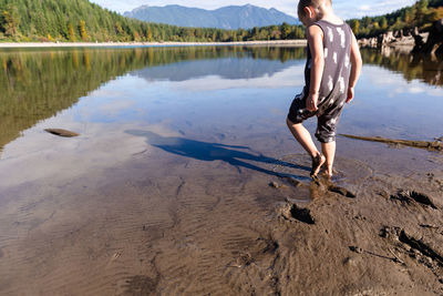 Young child plays barefoot in the mud near a lake in the sunshine