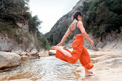 Young woman with braids jumping between the stones in the river