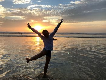 Man with arms outstretched at beach against sky during sunset