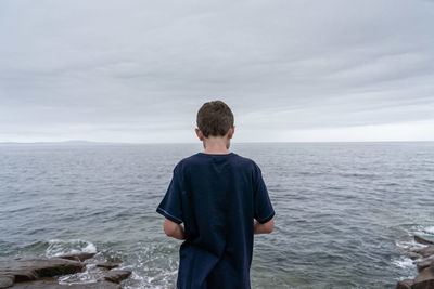 Rear view of boy standing in sea against sky