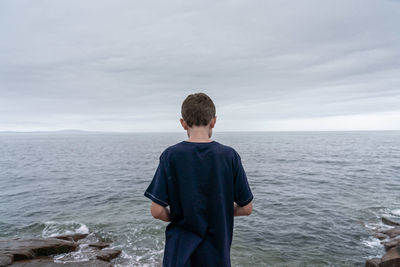 Rear view of boy standing at beach against sky