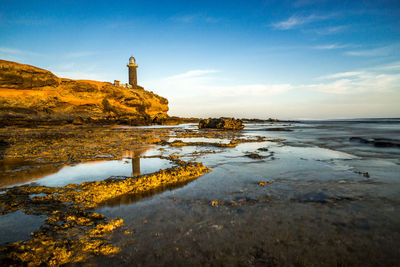 Lighthouse on beach by sea against sky