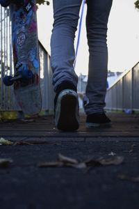 Low section of person walking with skateboard on footbridge