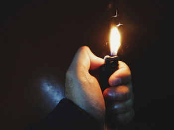 Close-up of hand holding lit candle in darkroom