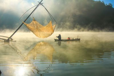 Men on fishboat in lake against sky