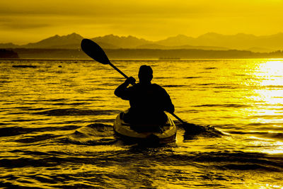 Silhouette man kayaking in sea against sky during sunset