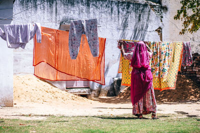 Rear view of woman drying clothes on clothesline against house