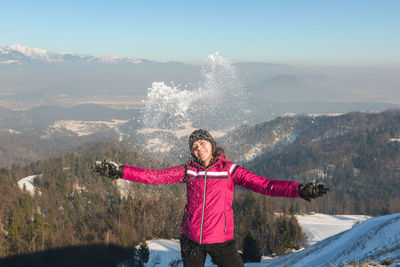 Woman playing with snow against mountains