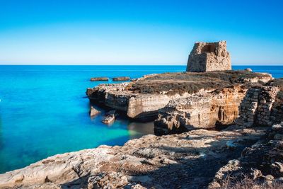 Scenic view of ancient totower over the sea against blue sky in salento