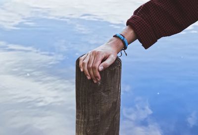 Cropped hand of man touching wooden post in lake