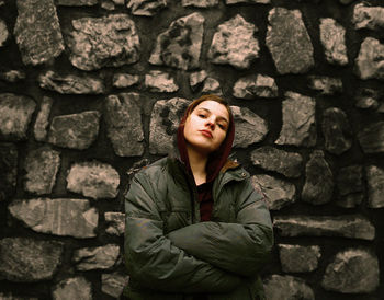 Portrait of confident woman with arms crossed standing against stone wall