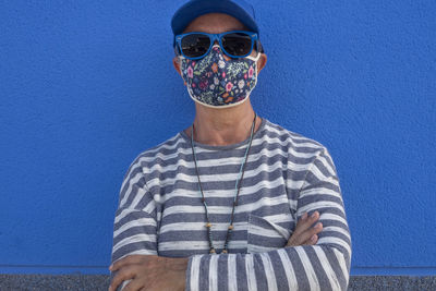 Portrait of young man wearing sunglasses standing against blue wall