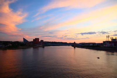 Silhouette buildings by river against sky during sunset