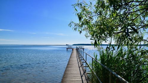 Wooden railing by sea against sky