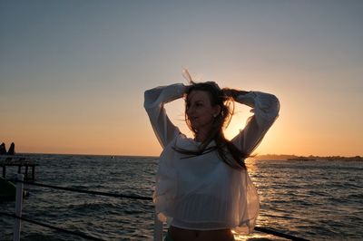 Woman standing by sea against sky during sunset