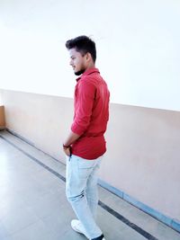 Side view of young man looking away while standing against wall