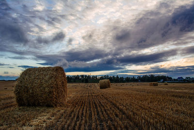 Hay bales at farm against cloudy sky