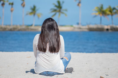 Rear view of woman sitting on sand at beach