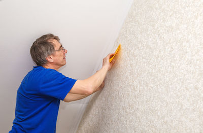 Side view of painter putting wallpaper on wall at construction site