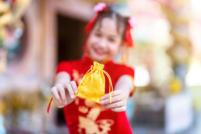 Portrait of smiling girl holding golden bag while sanding outdoors