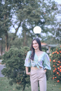 Portrait of smiling young woman standing against plants