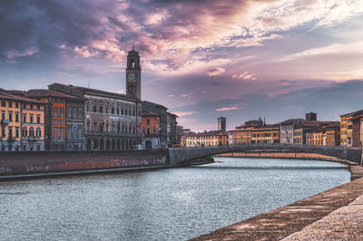 Bridge over river against buildings and dramatic sky in city of pisa